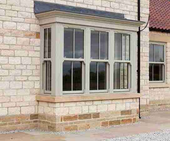 exterior of traditional sandstone home with green vertical slider windows